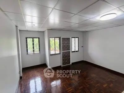Spacious empty room with wooden flooring and large windows, perfect for customization.