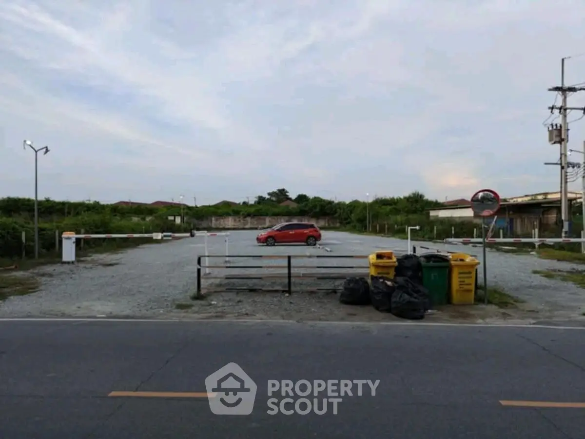 Spacious parking lot with a single red car and recycling bins, ideal for commercial use.