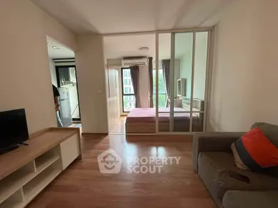 Modern apartment interior with cozy living room and bedroom separated by glass doors, featuring wooden flooring.