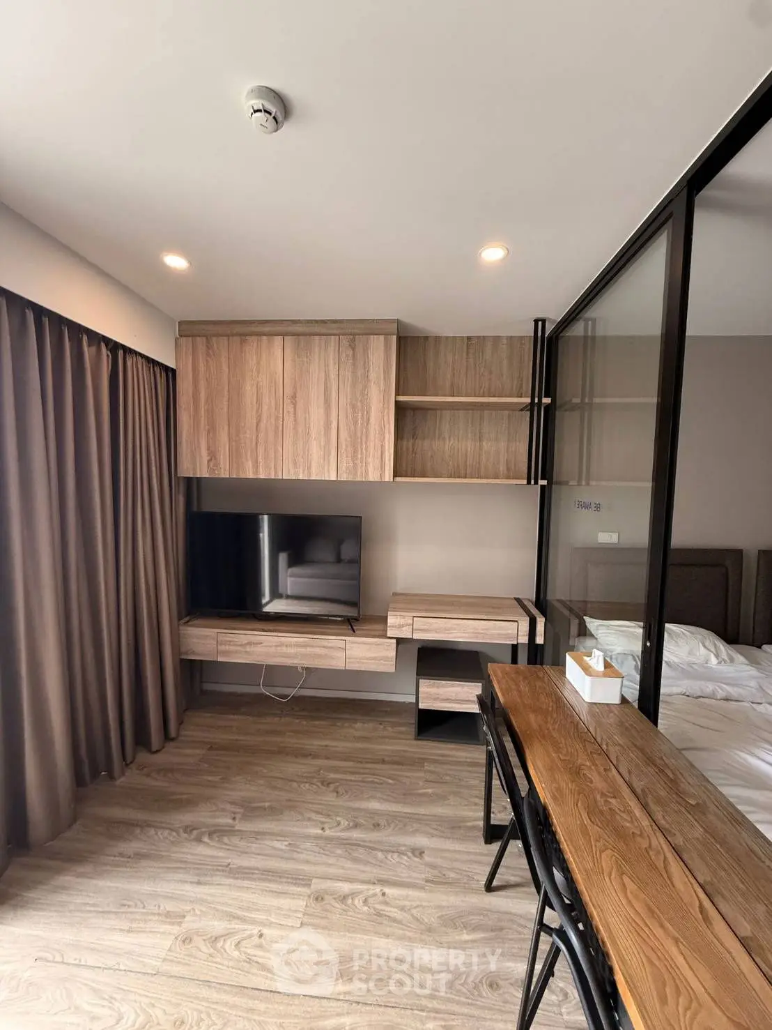 Modern bedroom with wooden flooring, built-in TV unit, and glass partition.