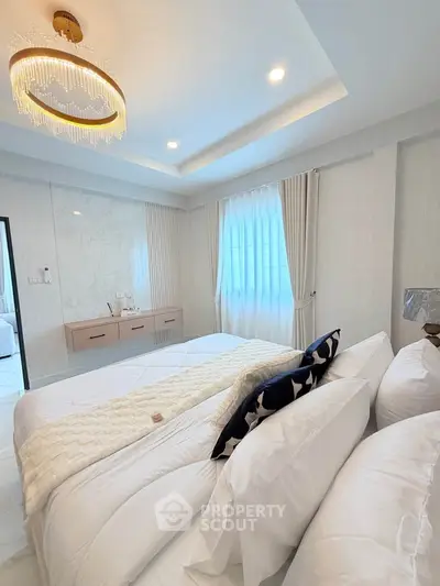 Luxurious bedroom with elegant chandelier and plush bedding in modern apartment.