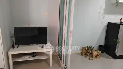 Modern living room with TV and sliding glass door leading to a bright space.