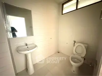 Spacious bathroom with pedestal sink and toilet, featuring high window for natural light.