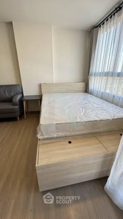 Modern bedroom with wooden flooring, bed, and natural light from large window.