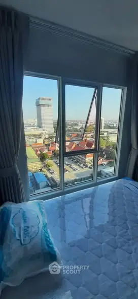 Bright bedroom with city view through large window, featuring a comfortable bed.