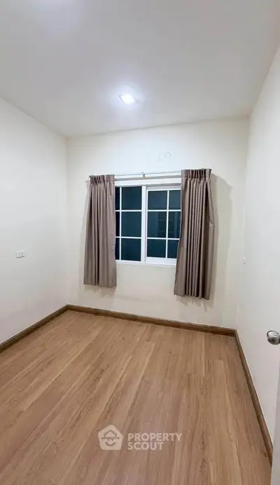 Spacious empty room with wooden flooring and large window, perfect for customization.