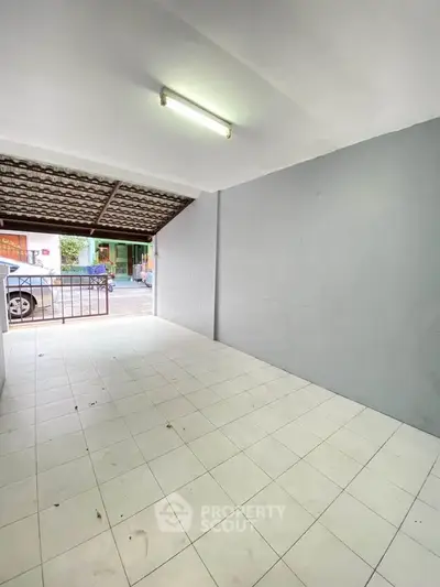 Spacious tiled garage area with covered roof and street view, ideal for parking or storage.