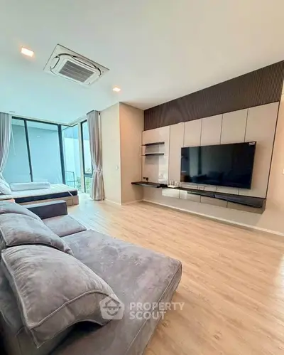 Spacious modern living room with large TV and cozy seating area, featuring floor-to-ceiling windows.