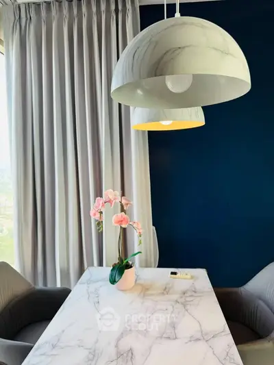Elegant dining area with marble table and modern pendant lights, featuring a chic orchid centerpiece.
