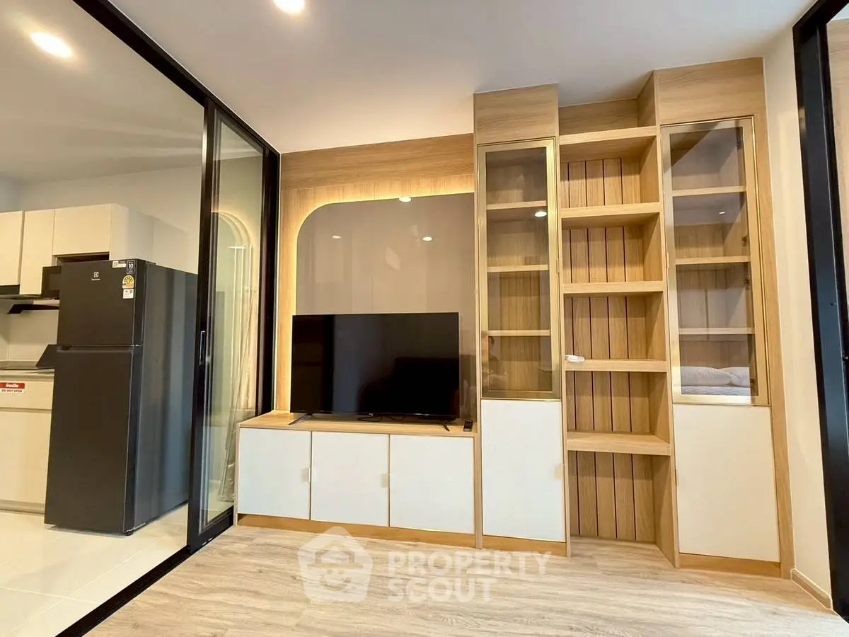 Modern living room with sleek TV unit and glass cabinets, adjacent to a stylish kitchen area.