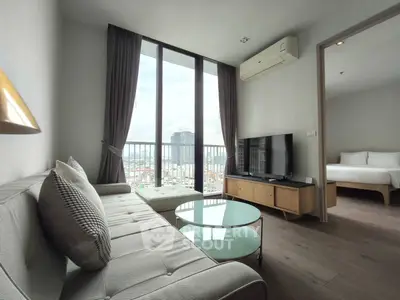 Modern living room with large windows and city view, featuring a cozy sofa and sleek TV setup.
