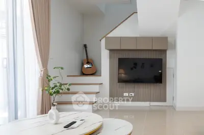 Modern living room with stylish decor, guitar on stairs, and large TV on wall.