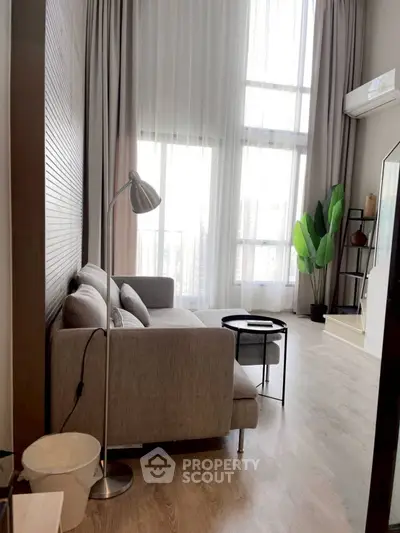 Modern living room with high ceilings and large windows offering city views.