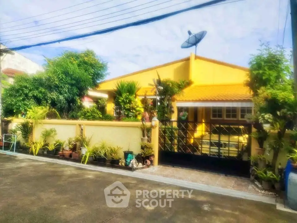 Charming yellow house with lush garden and secure gated entrance in a serene neighborhood.
