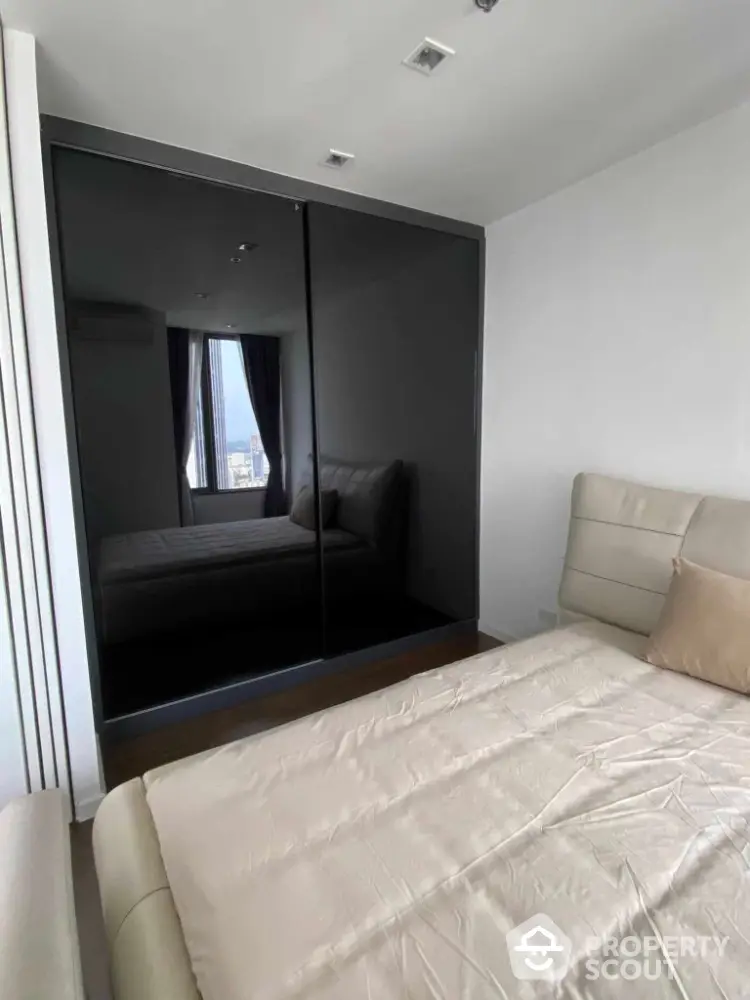 Modern bedroom with sleek mirrored wardrobe and city view window.