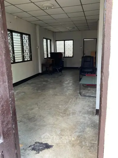 Spacious room with concrete floor and large windows, ideal for office or studio setup.