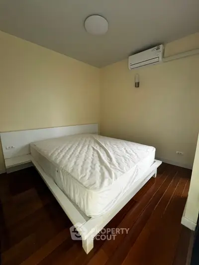Spacious bedroom with modern bed and air conditioning, featuring elegant wooden flooring.