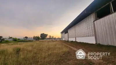 Expansive industrial warehouse with open field and serene sunset view.