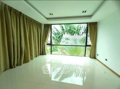 Spacious living room with large window and lush garden view, perfect for relaxation and natural light.