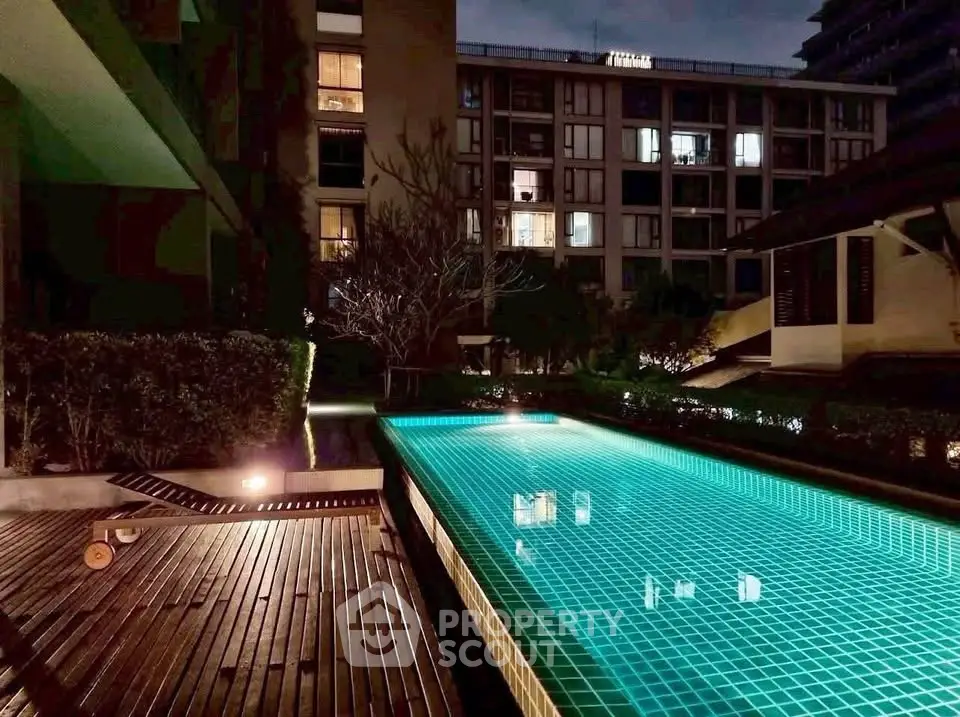 Luxurious night view of a modern apartment complex with illuminated swimming pool and elegant wooden deck.