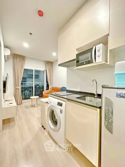 Modern apartment with open kitchen and living area, featuring washing machine and microwave.