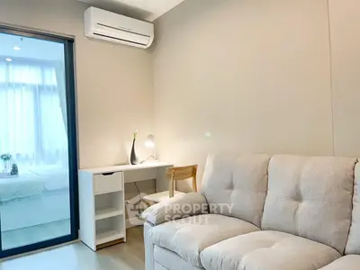 Cozy modern living room with plush sofa, sleek work desk, and ample natural light from large window, perfect for relaxation and productivity.