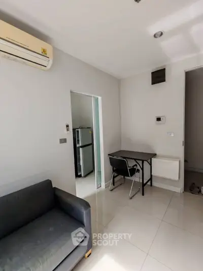 Modern living room with sleek furniture and air conditioning, adjacent to a compact kitchen.