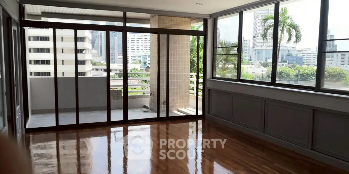 Spacious living room with large windows and balcony offering stunning city views.