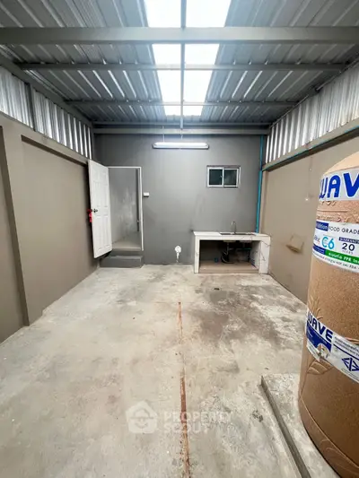 Spacious storage area with concrete floor and metal roof, featuring a sink and small window.
