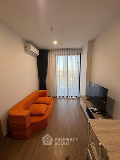 Modern living room with orange sofa and city view, featuring sleek wooden flooring and a wall-mounted TV.