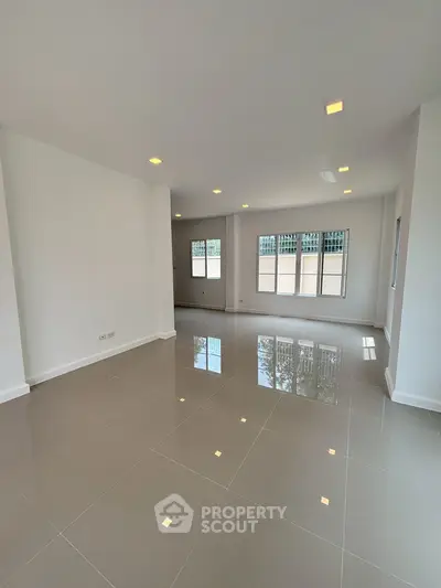 Spacious and bright empty living room with glossy tiled floors and large windows.