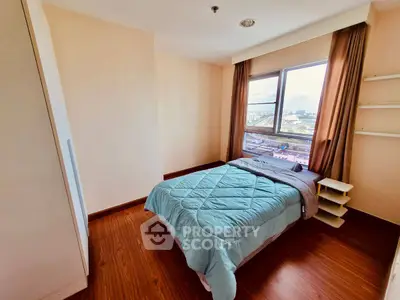 Cozy bedroom with city view and natural light, featuring wooden flooring and modern decor.