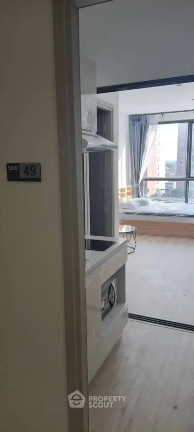 Modern apartment entrance with view into a bright bedroom featuring large windows and contemporary design.