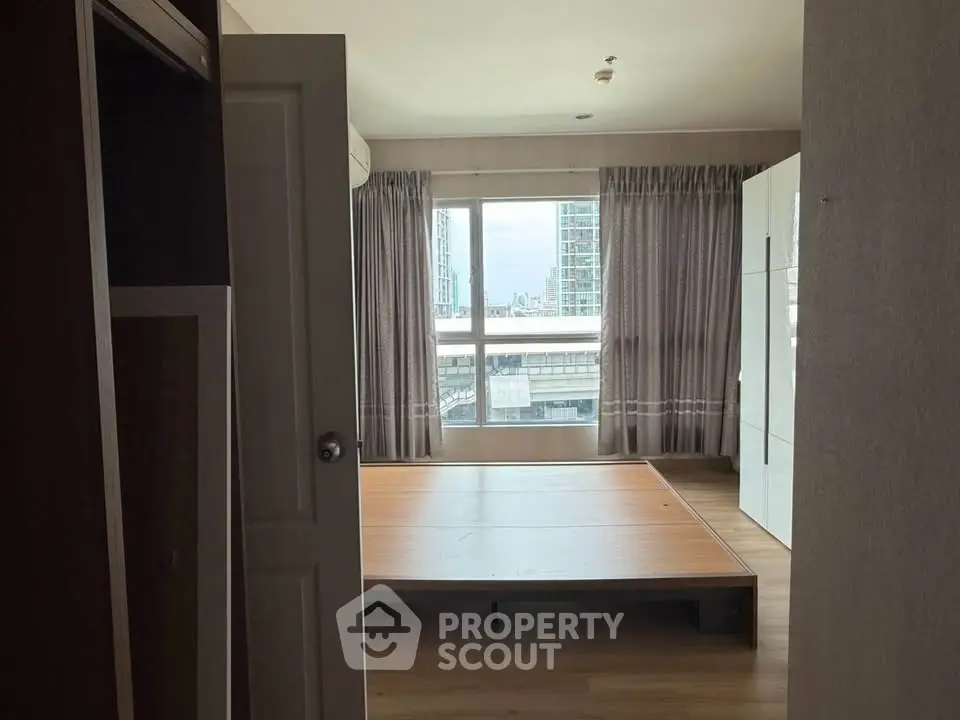 Spacious bedroom with large window and wooden flooring in modern apartment.