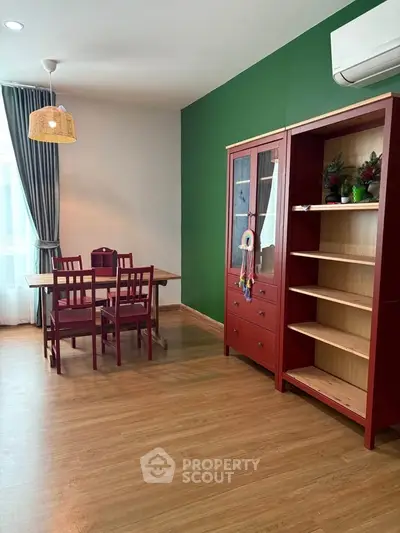 Charming dining area with wooden flooring, green accent wall, and elegant red furniture.