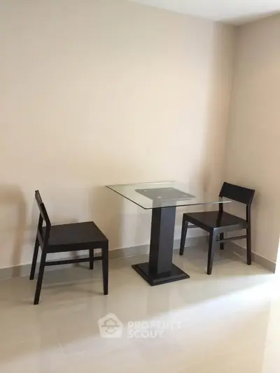 Minimalist dining area with glass table and two chairs in modern apartment.