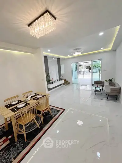 Spacious modern living room with elegant chandelier and dining area, featuring large windows and sleek flooring.
