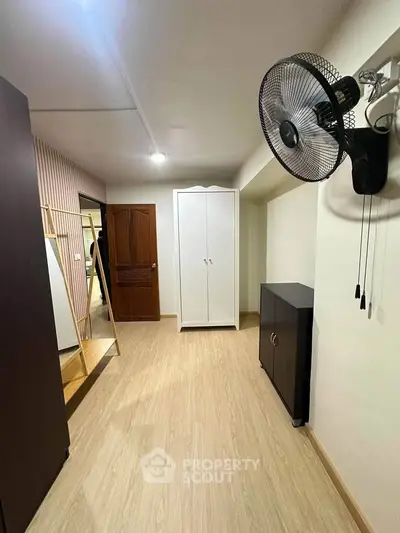 Spacious room with wooden flooring, wardrobe, and wall-mounted fan, ideal for versatile use.