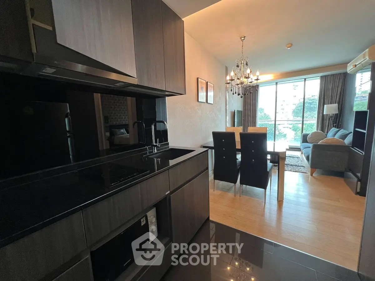 Modern open-plan kitchen and living room with elegant chandelier and large windows.