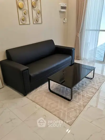 Modern living room with sleek black sofa and glass coffee table on elegant marble flooring.
