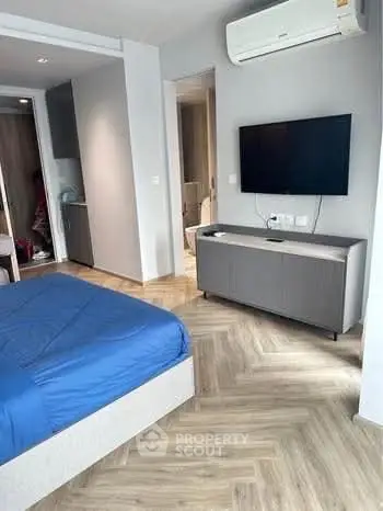 Modern bedroom with blue bedding, wall-mounted TV, and air conditioning in a stylish apartment.