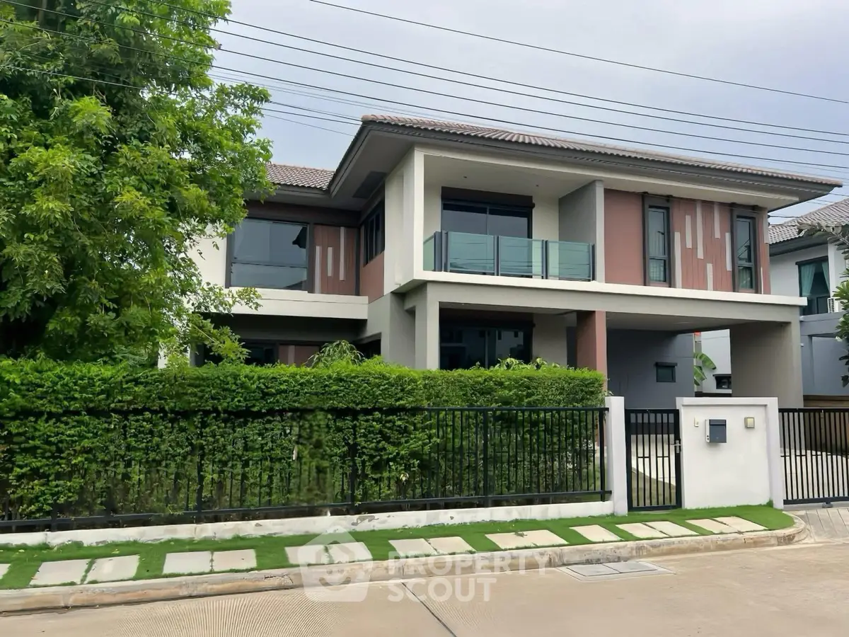Modern two-story house with lush greenery and sleek balcony in a serene neighborhood.