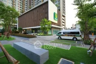 Modern urban apartment building with landscaped entrance and parking area.