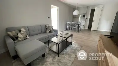 Spacious modern living room with elegant grey sectional sofa, sleek black coffee table, and an open layout leading to a well-equipped kitchen.