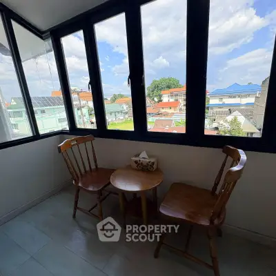 Charming enclosed balcony with wooden chairs and table, offering a scenic view of the neighborhood rooftops.