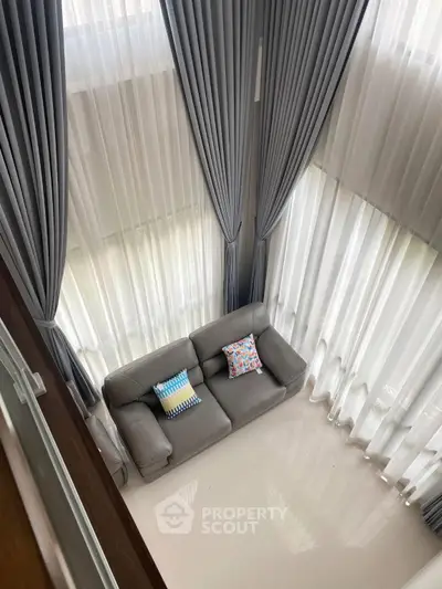 Luxurious high-ceiling living room with elegant curtains and cozy sofa, perfect for relaxation.