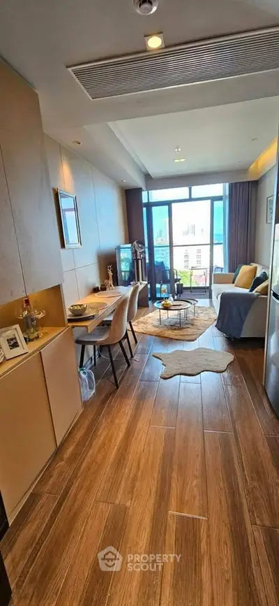 Modern living room with wooden flooring, stylish furniture, and large windows offering natural light.