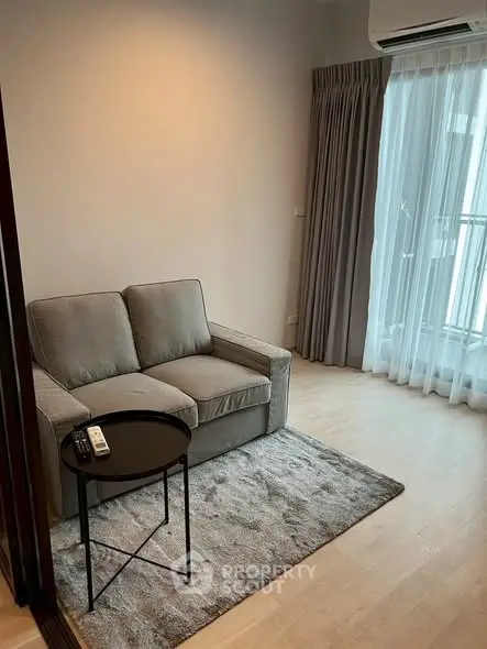 Cozy living room with modern sofa and natural light from large window, perfect for relaxation.