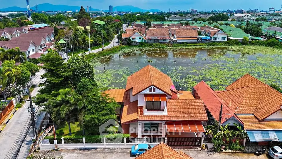 Charming suburban home with red-tiled roof overlooking serene pond and lush greenery.