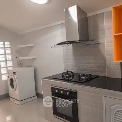 Modern kitchen with gas stove and washing machine in sleek design.
